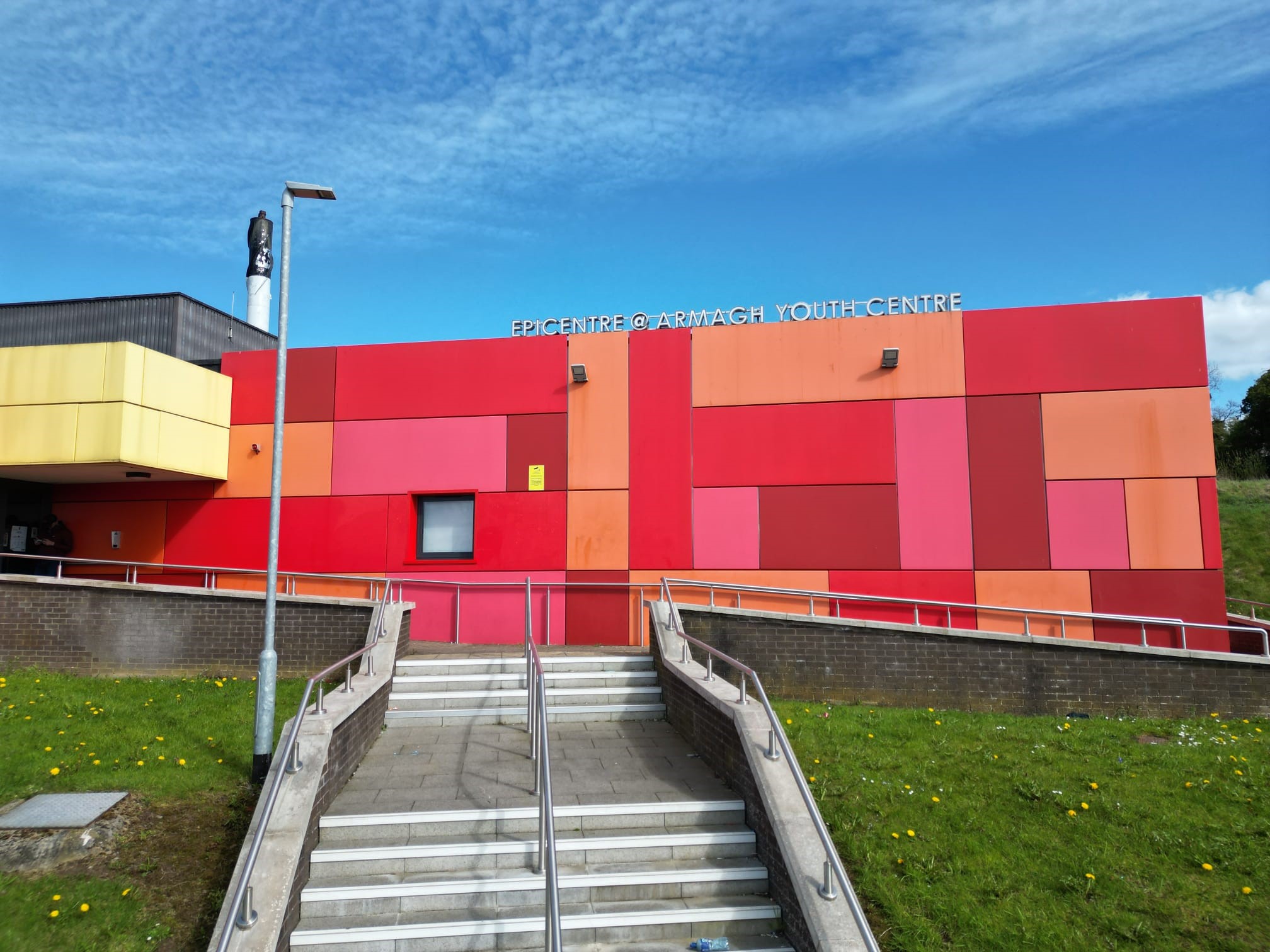 Front of epicentre. There are steps leading up to a large building which has red, pink, orange and yellow panels covering the whole building.