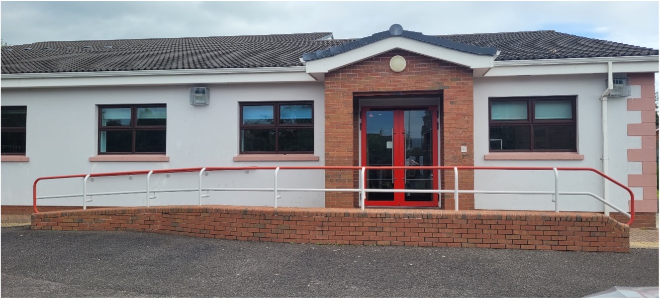 Front of Greenisland. There is a red door straight ahead and the building is cream. The window sills are painted red.