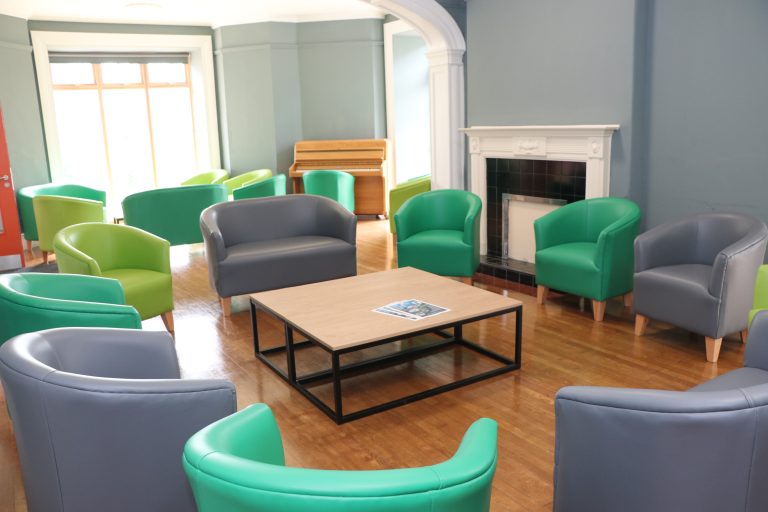 Common room with soft seating in a circle and a coffee table. There is a piano in the distance