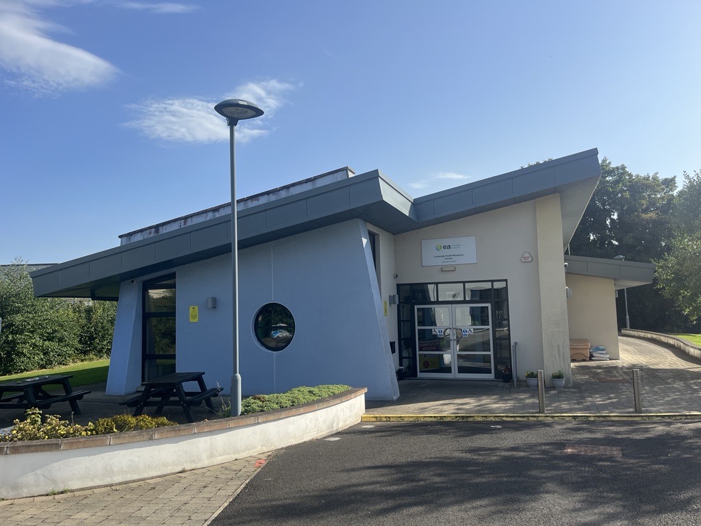 Front of Limavady Youth Resource Centre. The building has a slanted roof. One wall is pale blue and the other is cream. There is a circular window at the front.